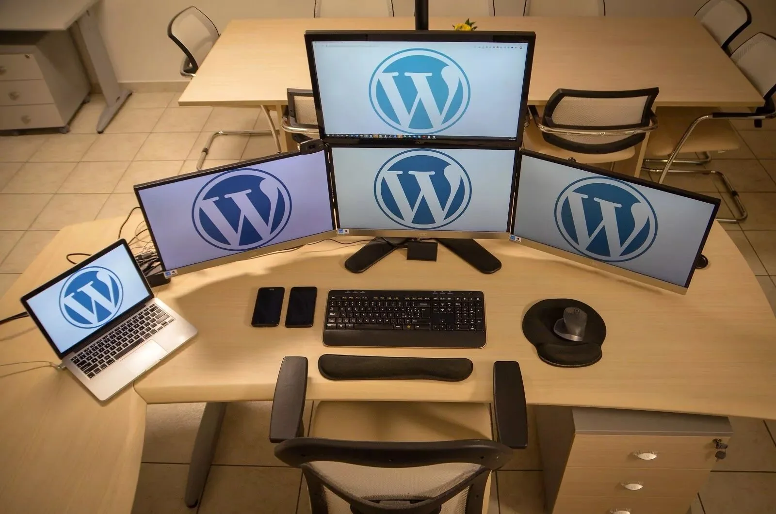 A curved desk with four monitors and a laptop, each screen showing the WordPress logo, with keyboard, mouse and desk speakers